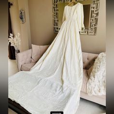 a white wedding dress hanging on a hanger in front of a couch and mirror