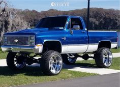 a blue and white truck parked on top of a grass covered field next to a street