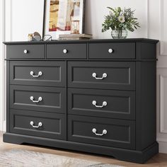 a large black dresser with drawers in a room next to a plant and framed photograph