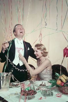 a man and woman standing next to each other at a table with streamers in the air