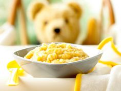 a teddy bear sitting next to a bowl of food on a white tablecloth with yellow trim