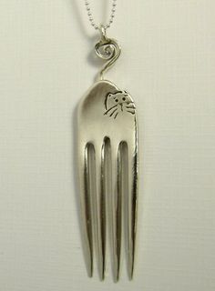 a fork with a cat on it is hanging from a necklace that has a chain attached to it