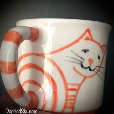 an orange and white coffee cup with a cat on it