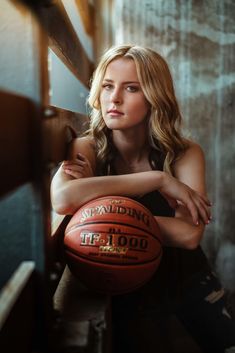 a woman leaning against a wall with a basketball in her hand and looking at the camera