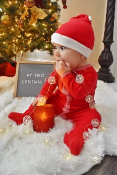 a baby wearing a santa hat sitting in front of a christmas tree