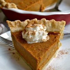 a slice of pumpkin pie on a plate with a fork and bowl in the background