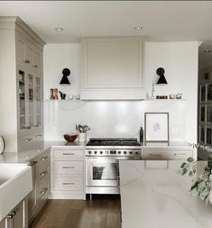 a white kitchen with marble counter tops and stainless steel appliances, along with wooden flooring