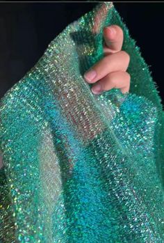 someone is holding onto a green sequined cloth with their hand on the fabric