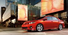 a red car parked in front of a tall building with large windows and an advertisement on it's side