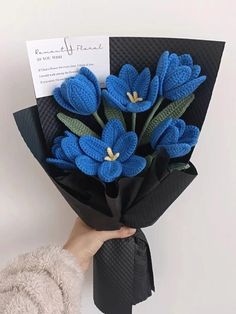 a hand holding a bouquet of blue crocheted flowers with a note attached to it