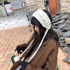 a woman sitting on a green chair wearing a white knitted hat and holding a cell phone