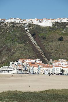 a beach with buildings on the hill and people walking along it