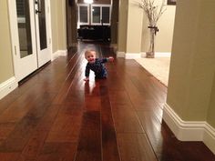 a toddler crawling on the floor in a hallway with hard wood floors and white trim