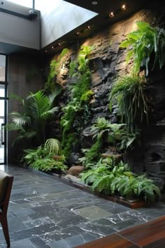 a living room filled with lots of green plants and greenery next to a stone wall