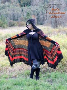 a woman is standing in the grass wearing a black and orange knitted shawl