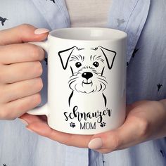 a woman holding a white coffee mug with a dog's face on it and the words schnauzer mom