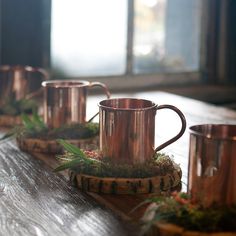 three copper mugs sitting on top of a wooden table with moss growing in them