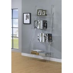 a clear shelf with books on it in front of a gray wall and wooden floor