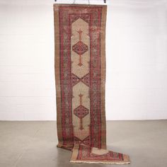 an old rug hanging on a wall in a room with white walls and tile flooring