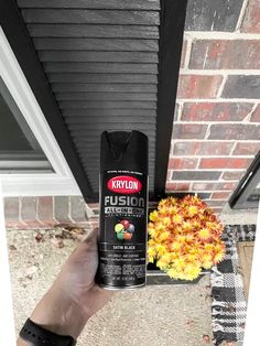 a person holding a spray can in front of a brick house with flowers on the porch