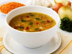 a white bowl filled with soup sitting on top of a table next to onions and garlic