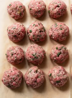 raw meatballs are lined up on a sheet of parchment paper and ready to be cooked