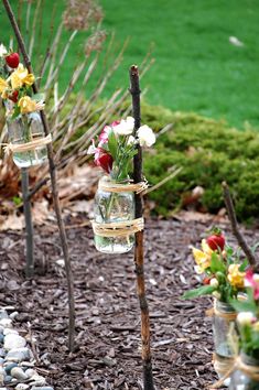 three mason jars filled with flowers on top of a rock garden path in front of a green lawn