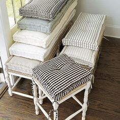 a stack of pillows sitting on top of a wooden floor next to a chair and ottoman