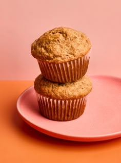 two muffins sitting on top of a pink plate next to an orange background