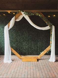 an outdoor ceremony setup with white draping and greenery on the wall behind it