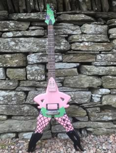 a pink and green guitar sitting on top of a pile of rocks next to a stone wall