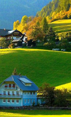 a large white house sitting in the middle of a lush green field with mountains behind it