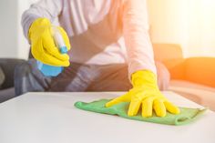 a person in yellow gloves cleaning a table with a green microfibrel cloth