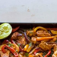 chicken fajita with peppers and onions on a sheet pan next to a lemon wedge