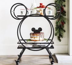 a mickey mouse cake is sitting on a stand in front of a christmas wreath and other decorations