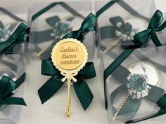 four clear boxes with green ribbons and brooches on the top one has a name tag attached to it