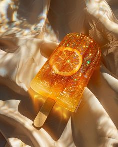 an orange ice lolly popsicle sitting on top of a white sheet covered in glitters