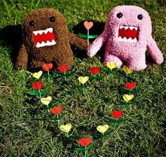 two stuffed animals sitting in the grass with hearts and flowers on it's feet