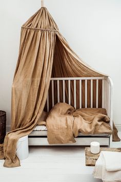 a white crib with a brown blanket on top of it next to pillows and blankets