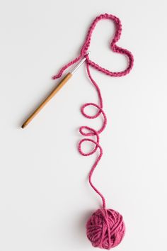 a ball of yarn and a knitting needle on a white surface with a heart - shaped crochet hook