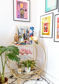 a gold bar cart filled with glasses and drinks on top of a rug next to pictures