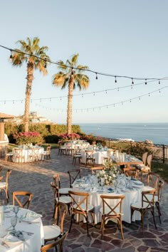 an outdoor dining area with tables and chairs set up for a formal dinner overlooking the ocean