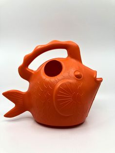 an orange vase with a fish design on the front and side, sitting on a white surface