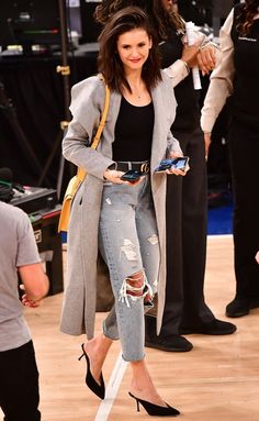 a woman standing on top of a wooden floor wearing ripped jeans and a gray coat