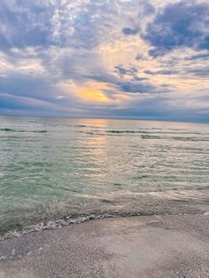 the sun is setting over the ocean with clouds in the sky and water on the beach