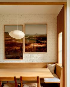 two paintings hang on the wall above a wooden table and bench in a room with white brick walls