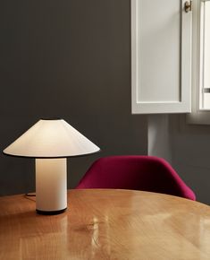 a table with a lamp on it next to a red chair in front of a window