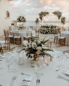 the table is set with white flowers and candles for an elegant wedding reception at the beach