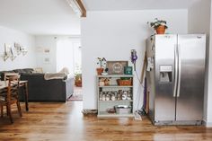 a kitchen and living room are shown with wood flooring in this photo, there is a stainless steel refrigerator next to the dining table