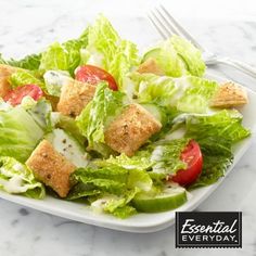 a salad with croutons and lettuce is on a plate next to a fork